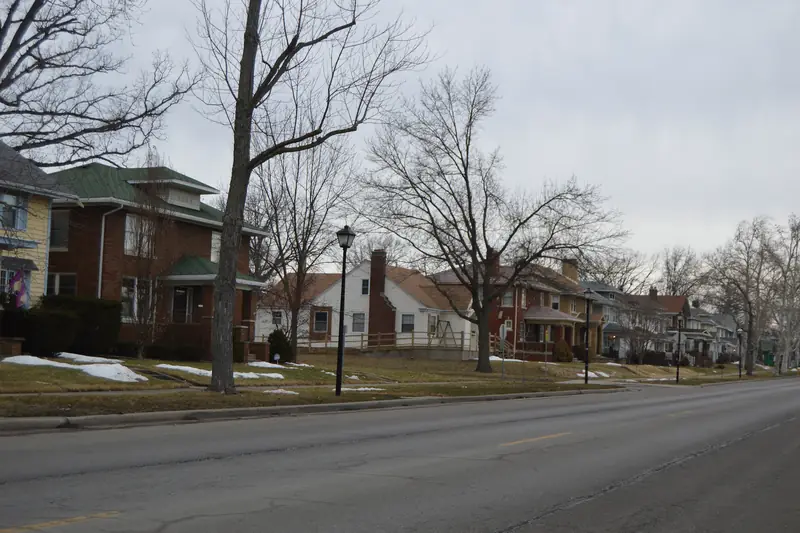 Older two-story frame houses set back behind bare trees on a broad Fort Wayne avenue, with snow on the grass