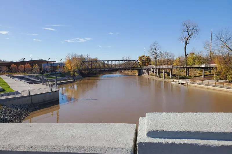 Silty brown river flowing past concrete riverfront steps toward an old steel truss bridge